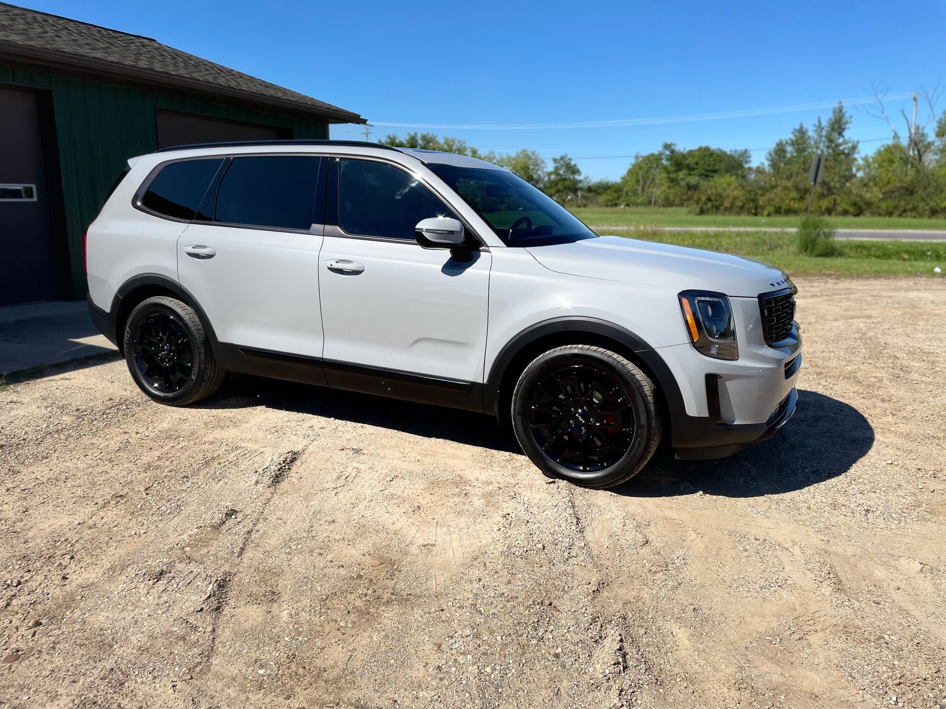 A white suv is parked in a gravel lot in front of a garage.