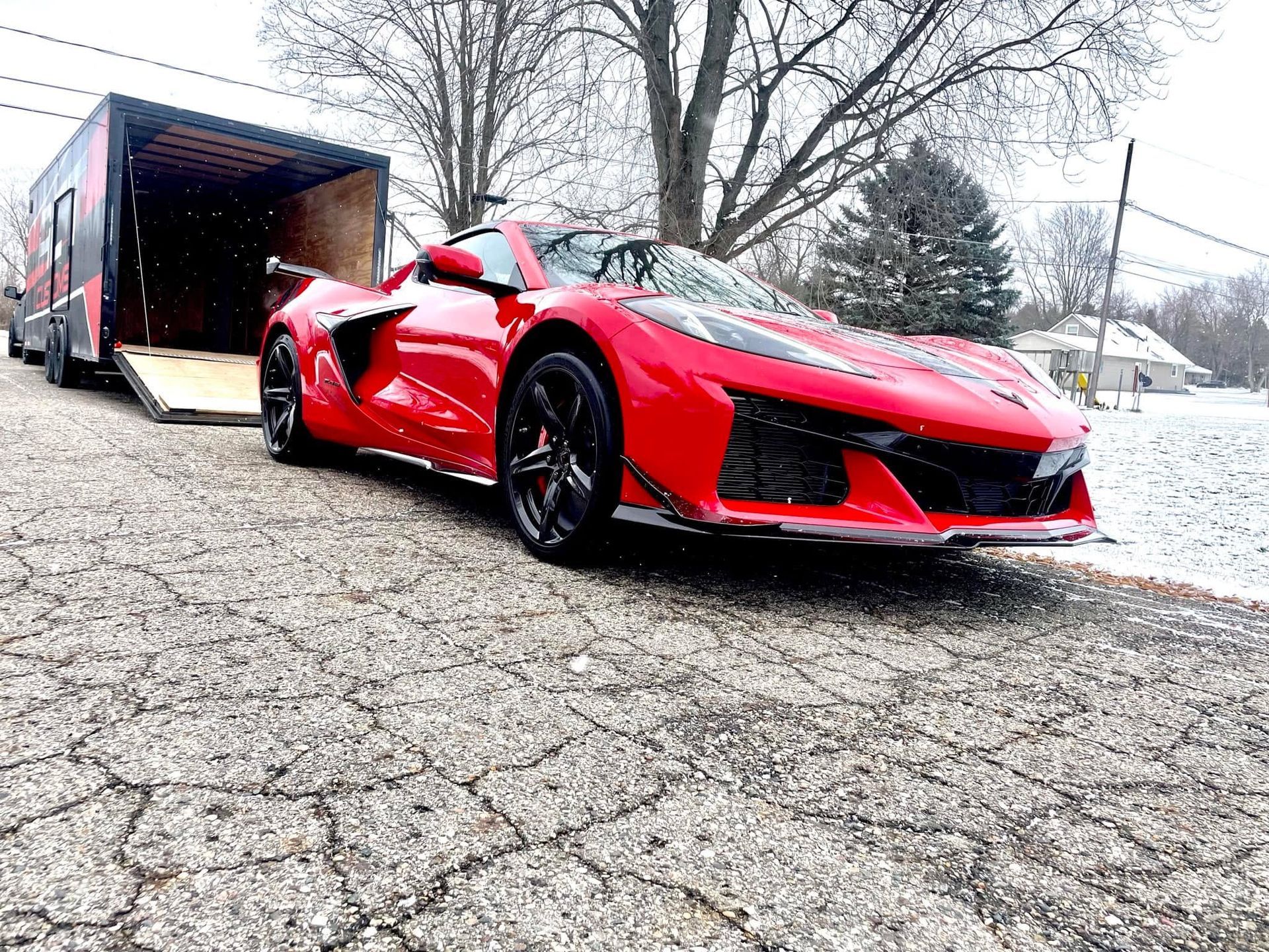 A red sports car is parked next to a trailer.