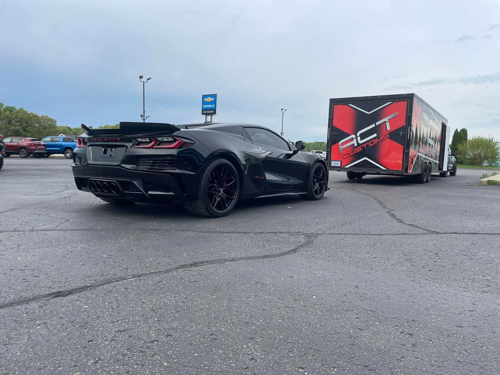 A black sports car is parked next to a red trailer in a parking lot.