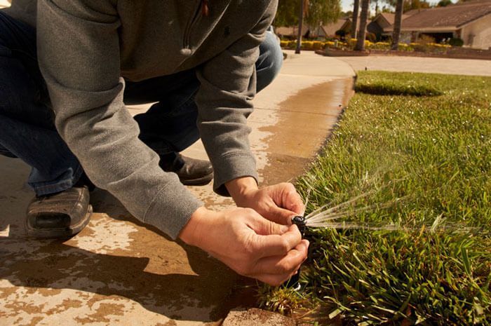 A man is kneeling down to fix a lawn sprinkler.