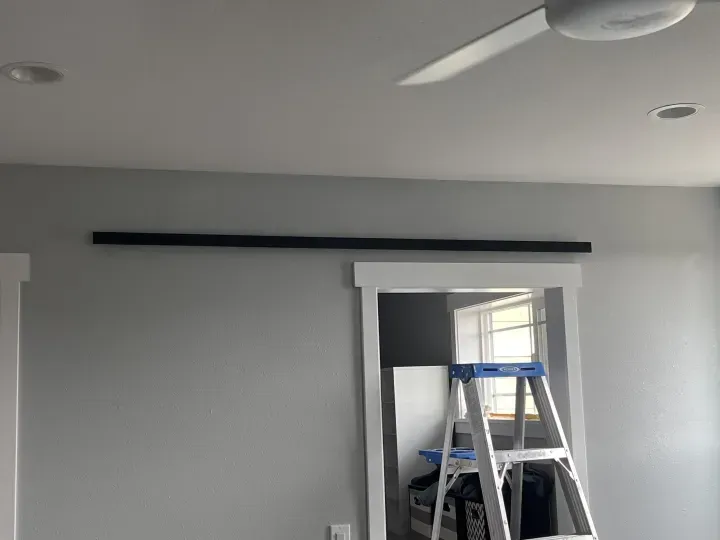 Black barn door track installed above a doorway, step ladder inside doorway, ceiling fan and recessed lighting.