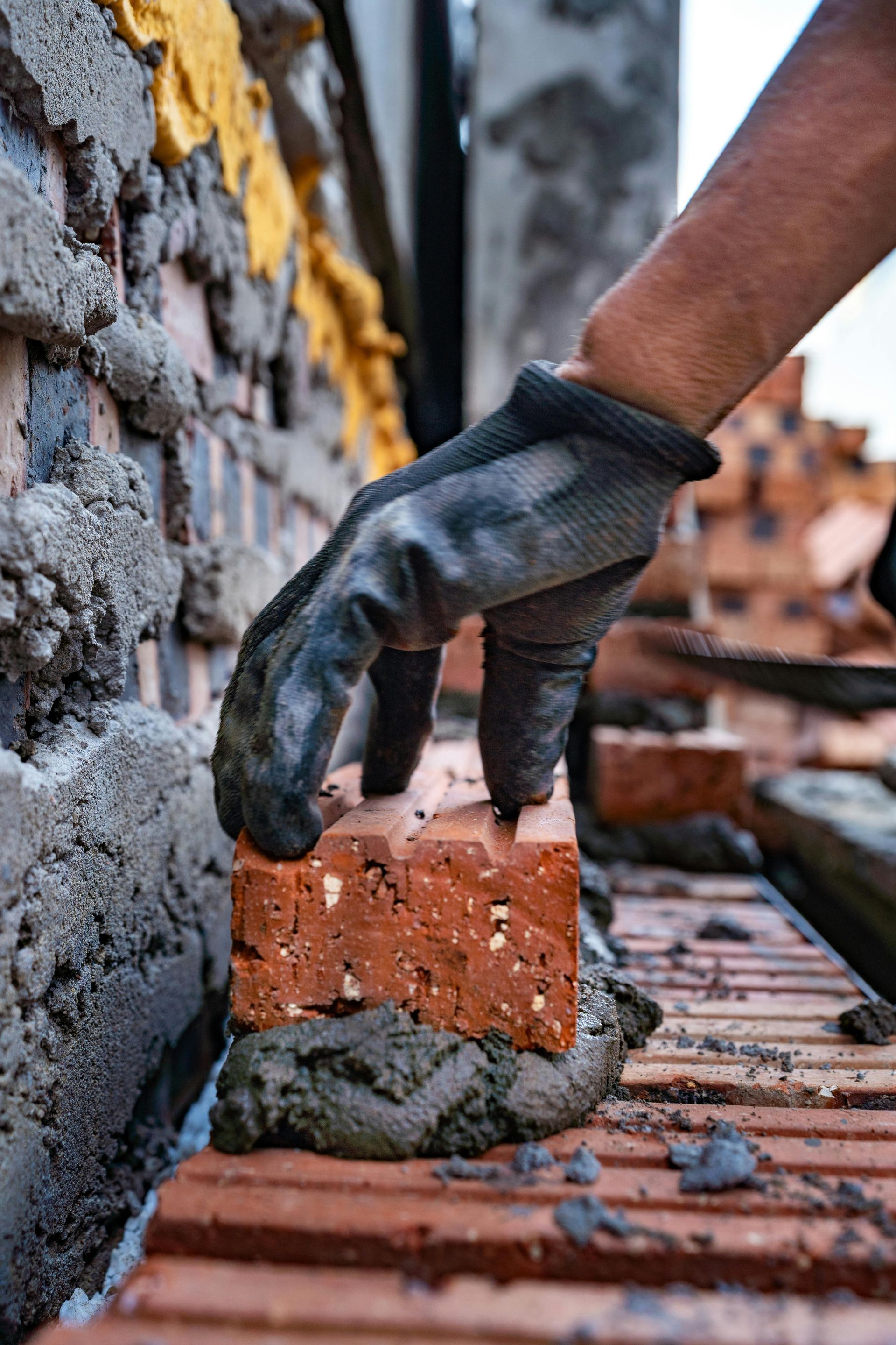 A gloved hand places a red brick on a mortar bed during bricklaying; close-up.