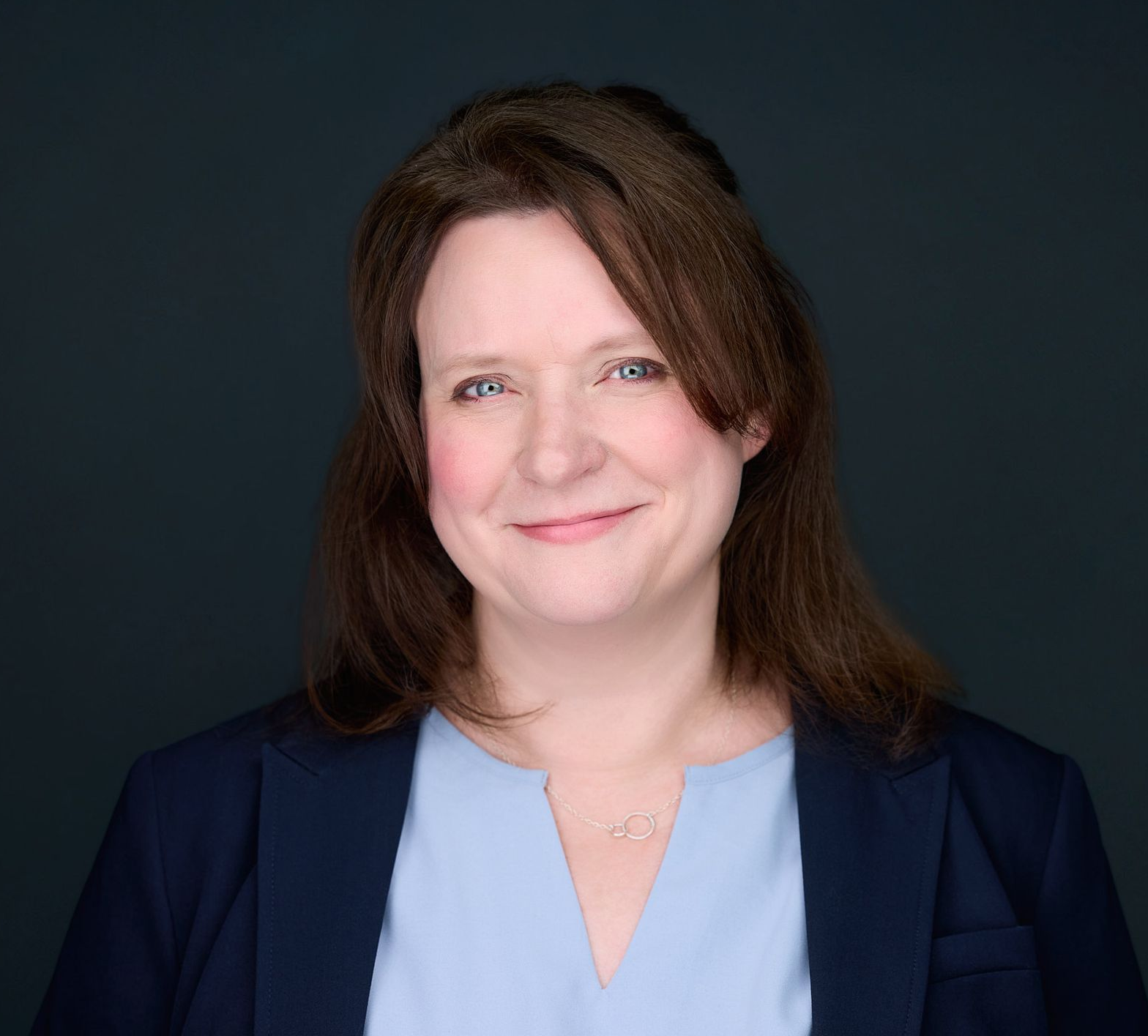 A woman wearing a blue striped shirt and a necklace is smiling for the camera.