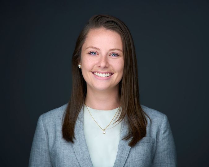 A woman in a suit and necklace is smiling for the camera.