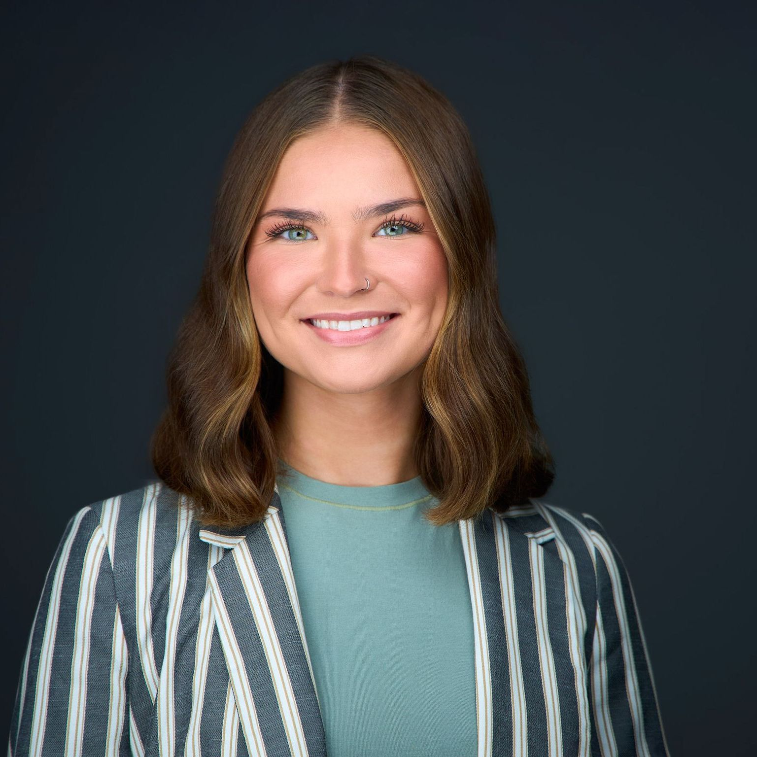 A woman is wearing a striped jacket and smiling for the camera.