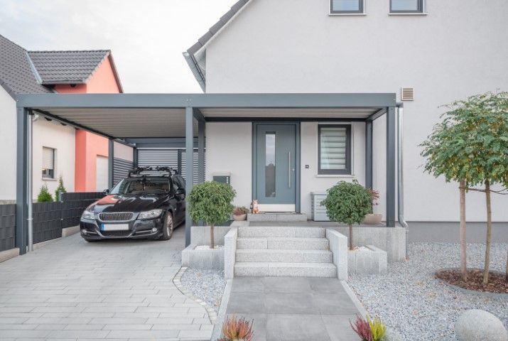 Modern house entrance with a carport, black car, front steps, and landscaped yard