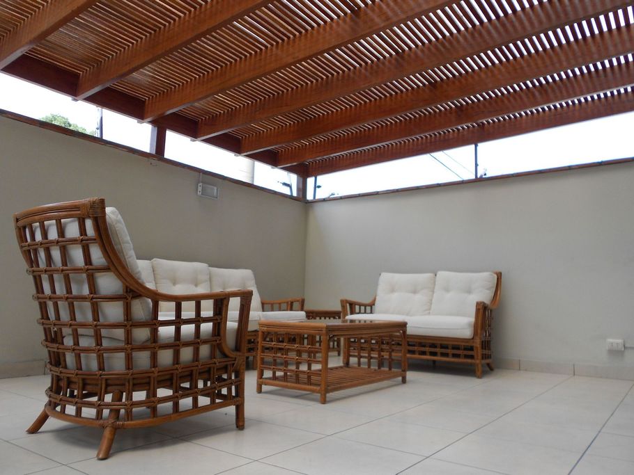 Patio seating area with wicker chairs, sofa, and coffee table under a wooden slat roof.