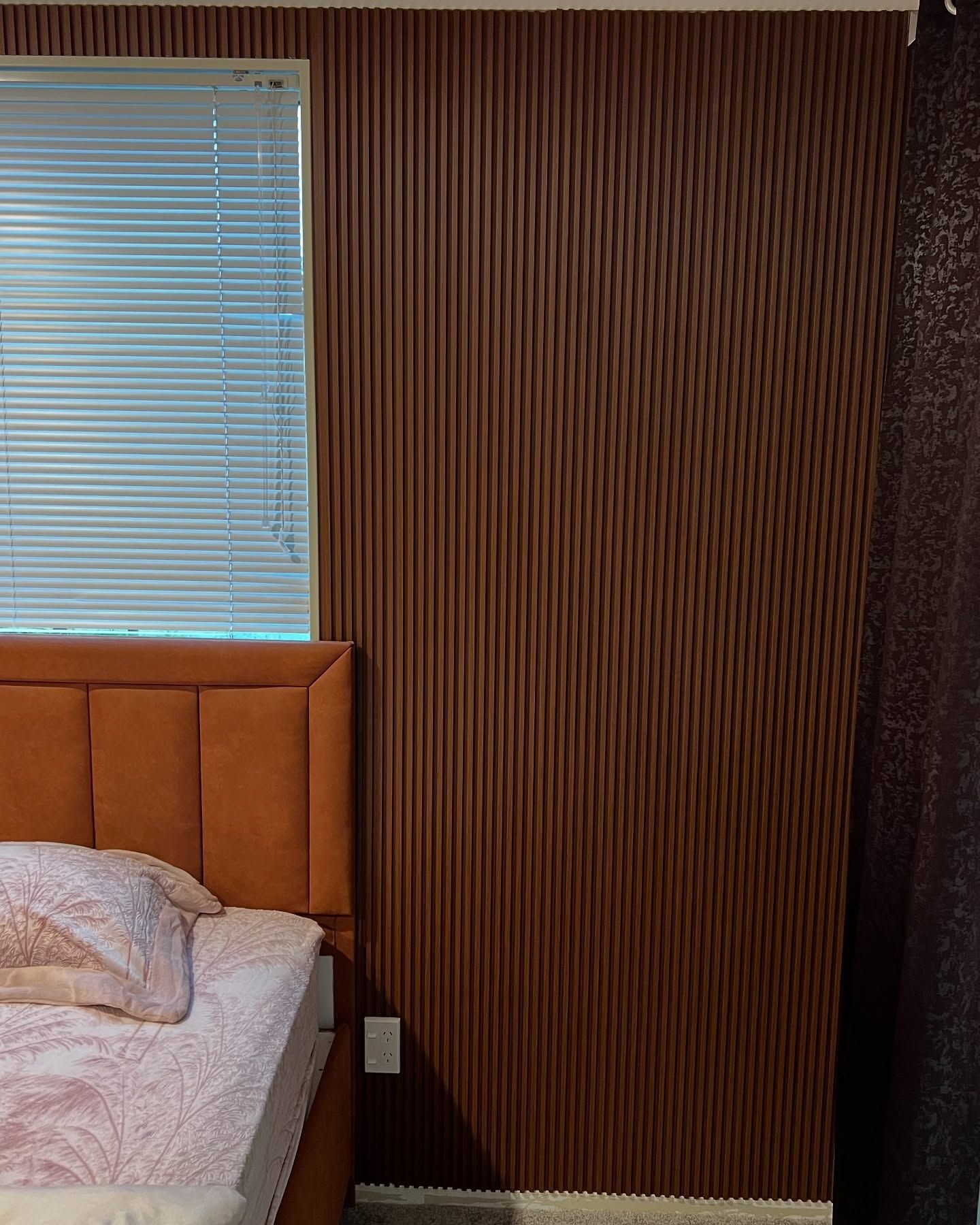 Bedroom with a brown, textured accent wall, bed with orange headboard, and a window with blinds.