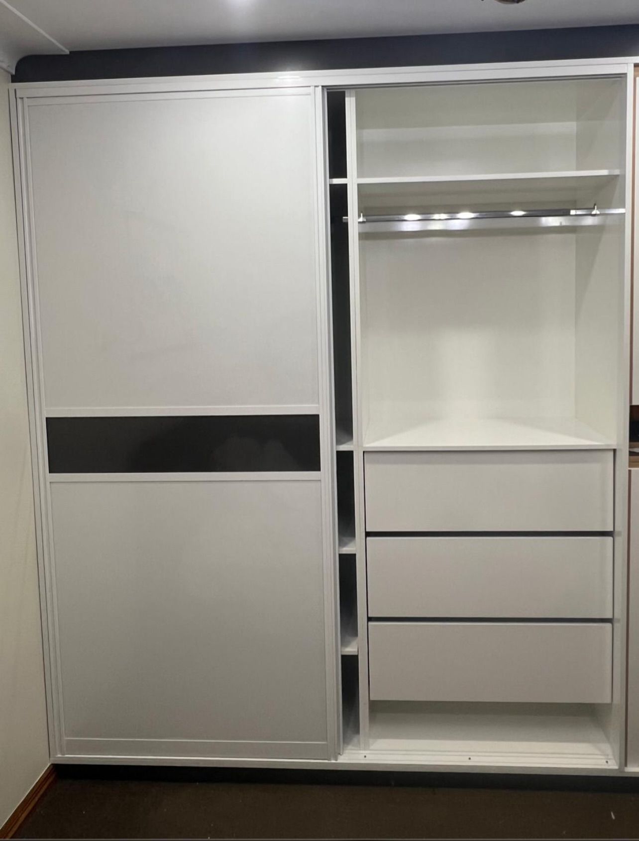 White sliding door closet with open section, featuring shelves, drawers, and a hanging rod.