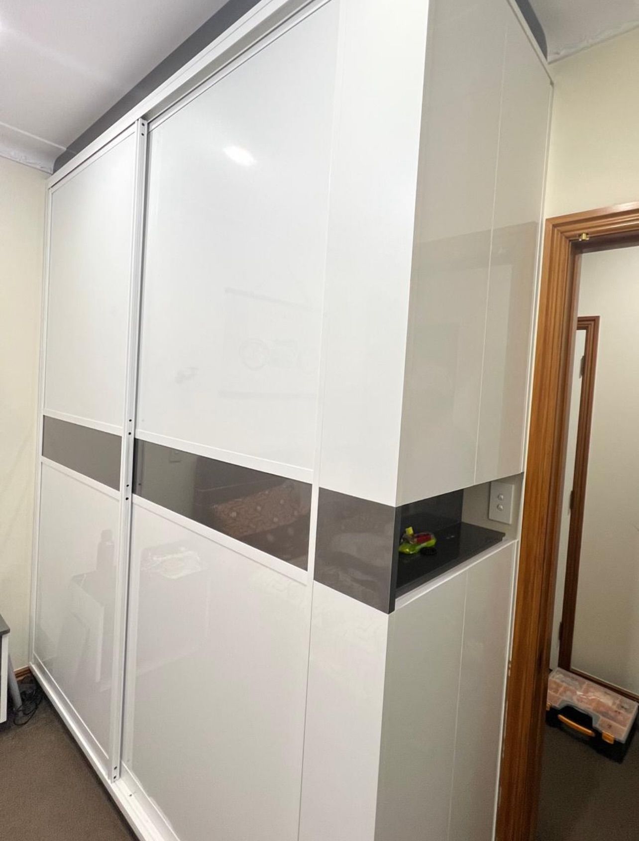 White sliding door wardrobe with a brown accent, next to an open doorway.