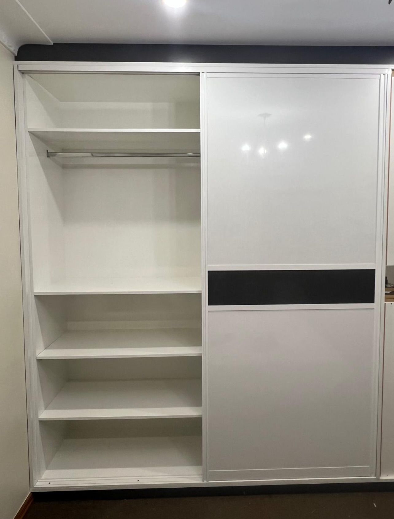 White closet with sliding doors, shelves, and a hanging rod. One door panel has a black stripe.