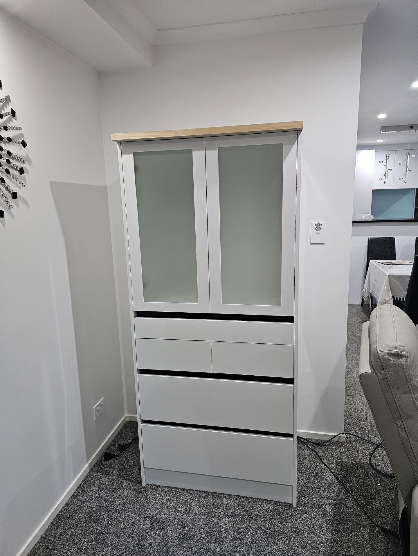 White cabinet with glass doors and drawers, wooden top, in a room with a rug and white walls.