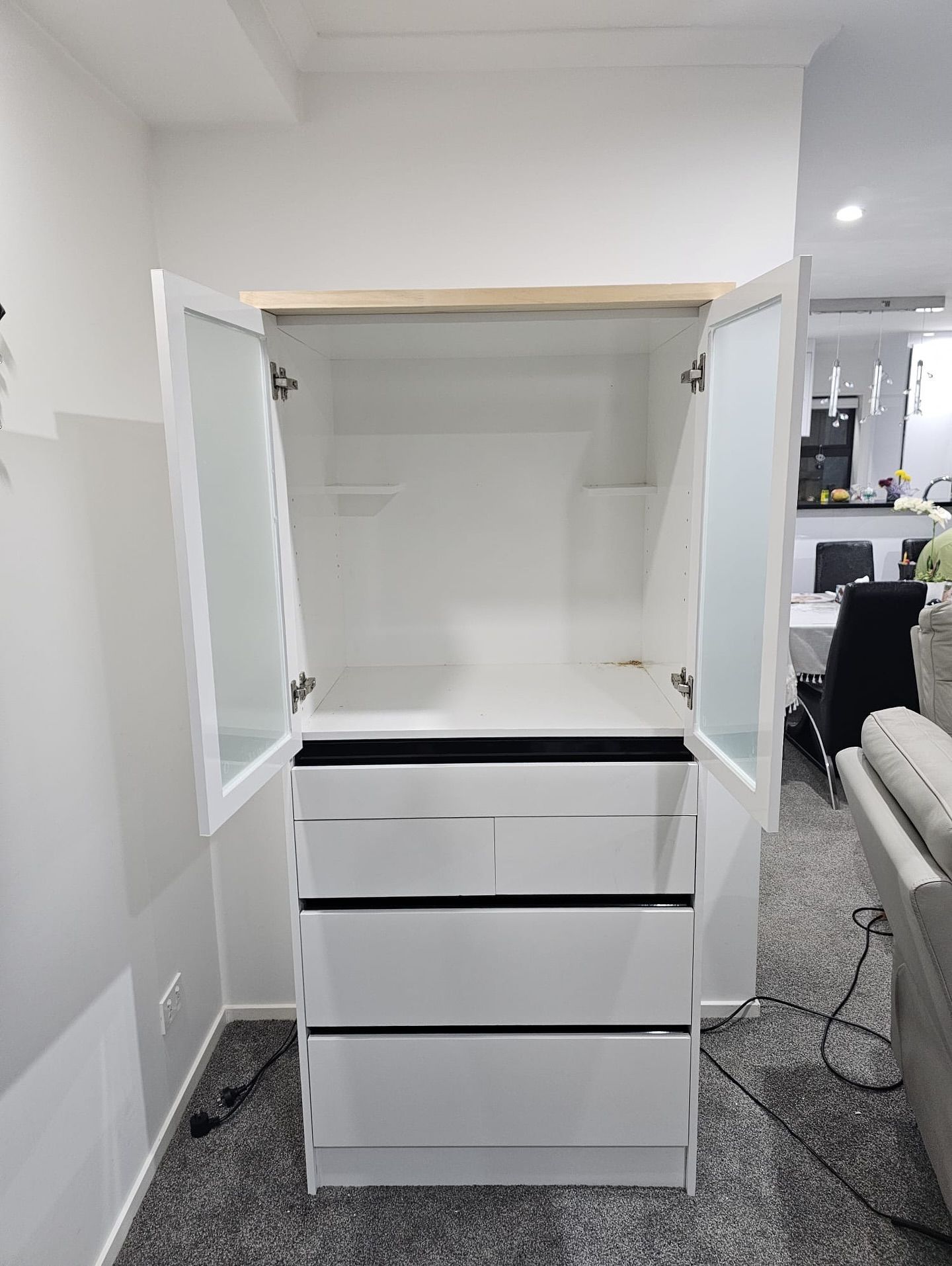 White cabinet with open doors and drawers, against a white wall in a room.