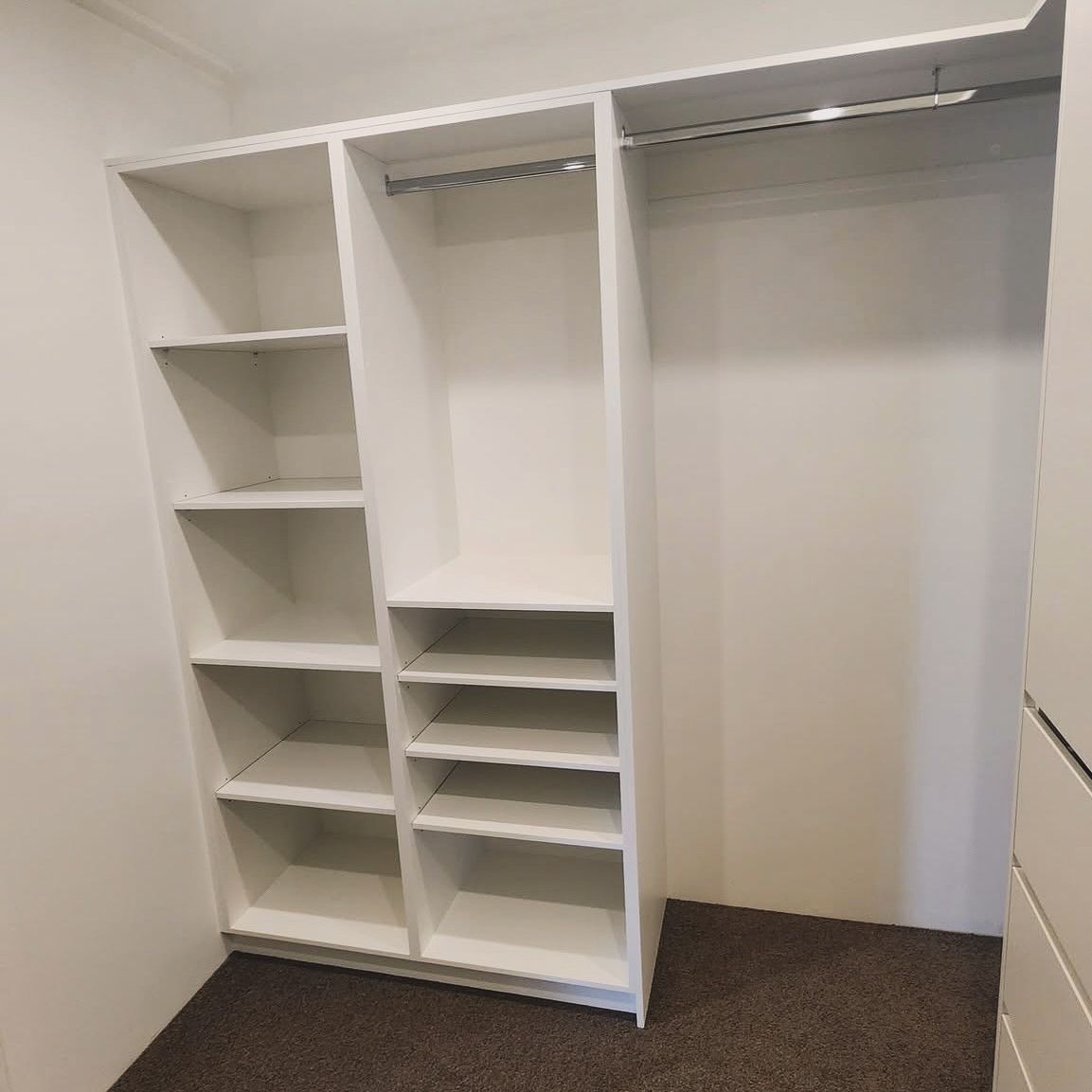 White built-in closet with shelves and hanging rod. Located in room with brown carpet.