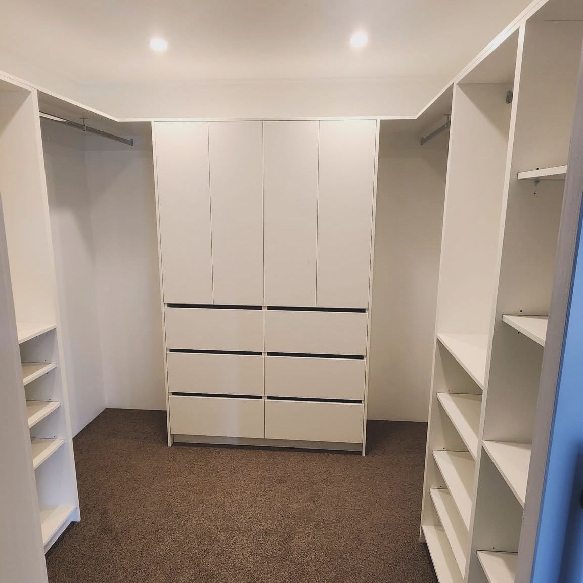 White walk-in closet with shelves and drawers. The carpet is brown, and the walls are white.