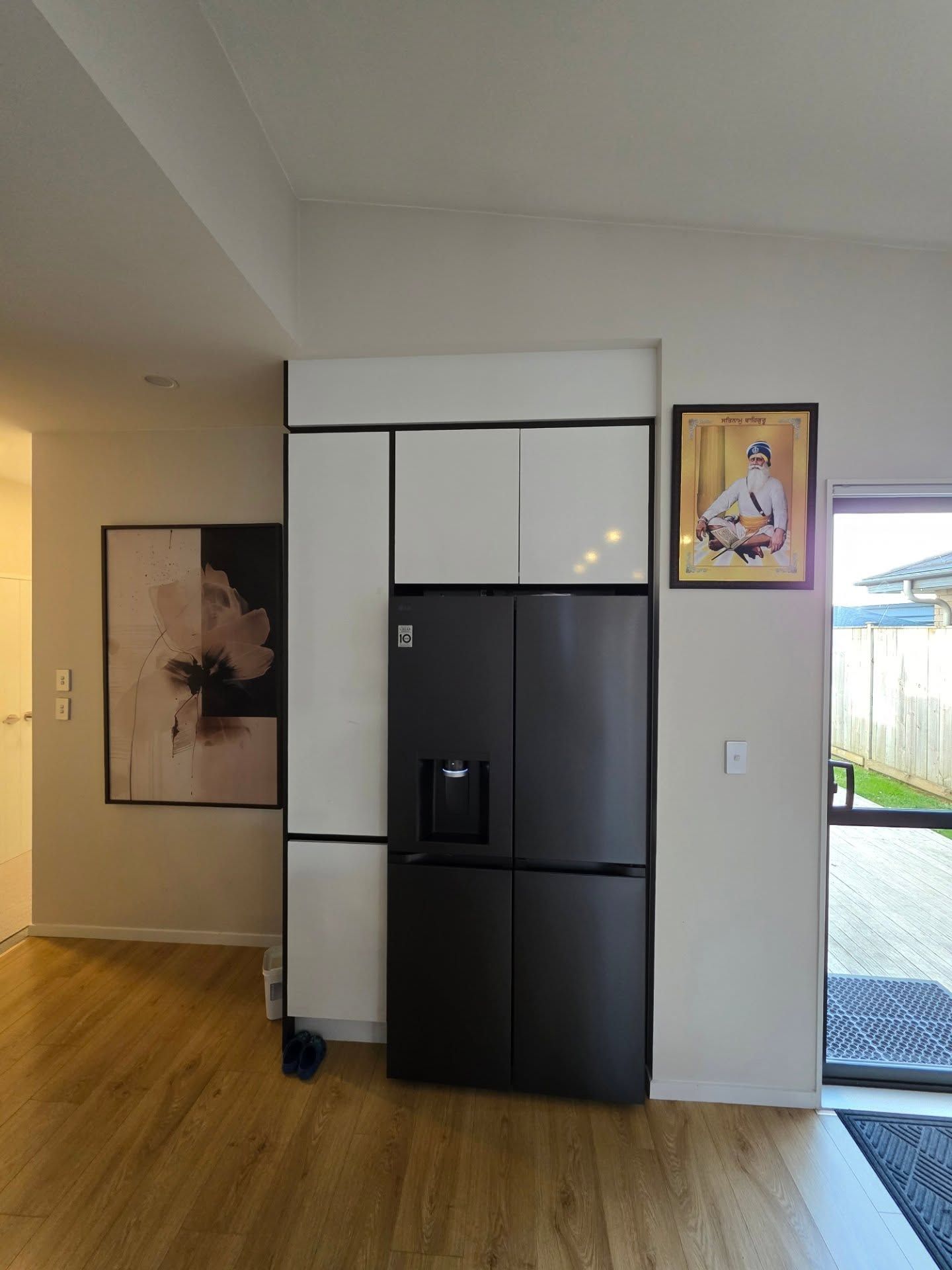 Black refrigerator built into white cabinetry. Artwork and framed print on adjacent walls.