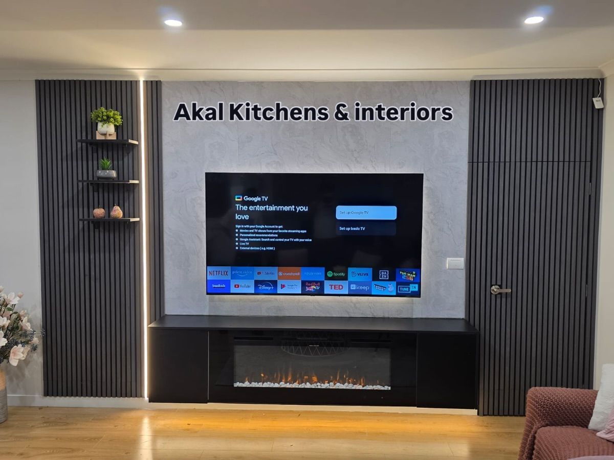 Living room with a large TV, fireplace, and built-in black storage unit. Gray textured paneling on the wall.