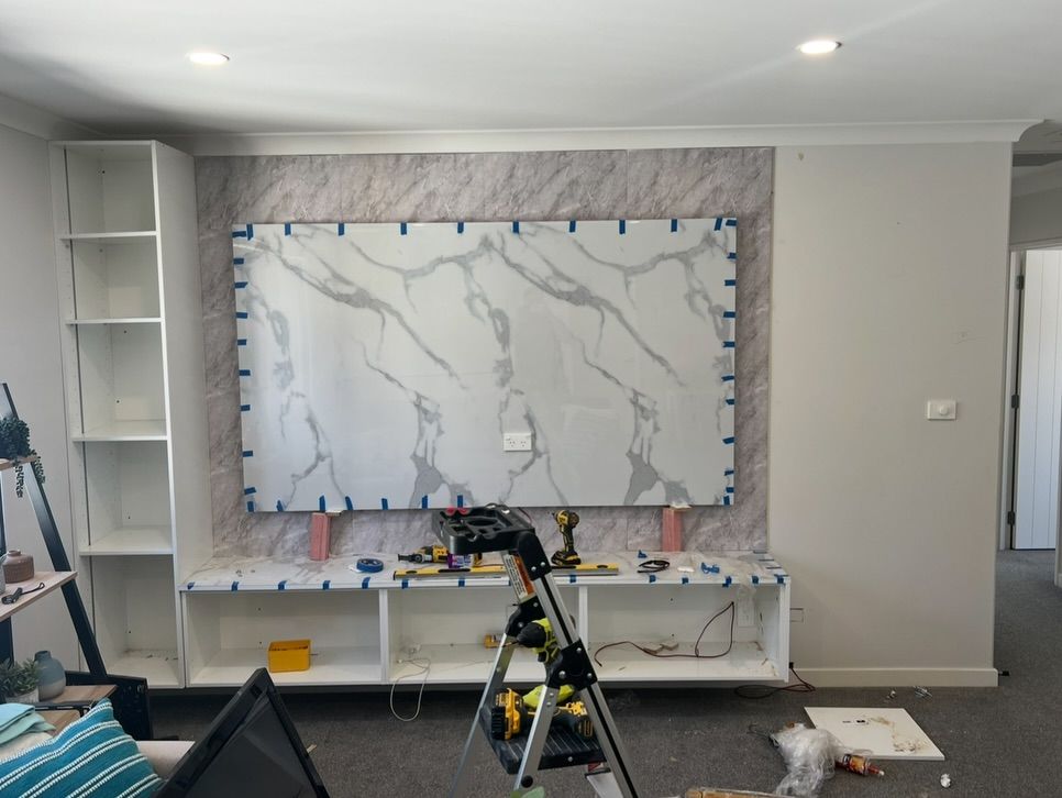 A living room with built-in cabinetry, a quartz panel feature wall, and construction tools.