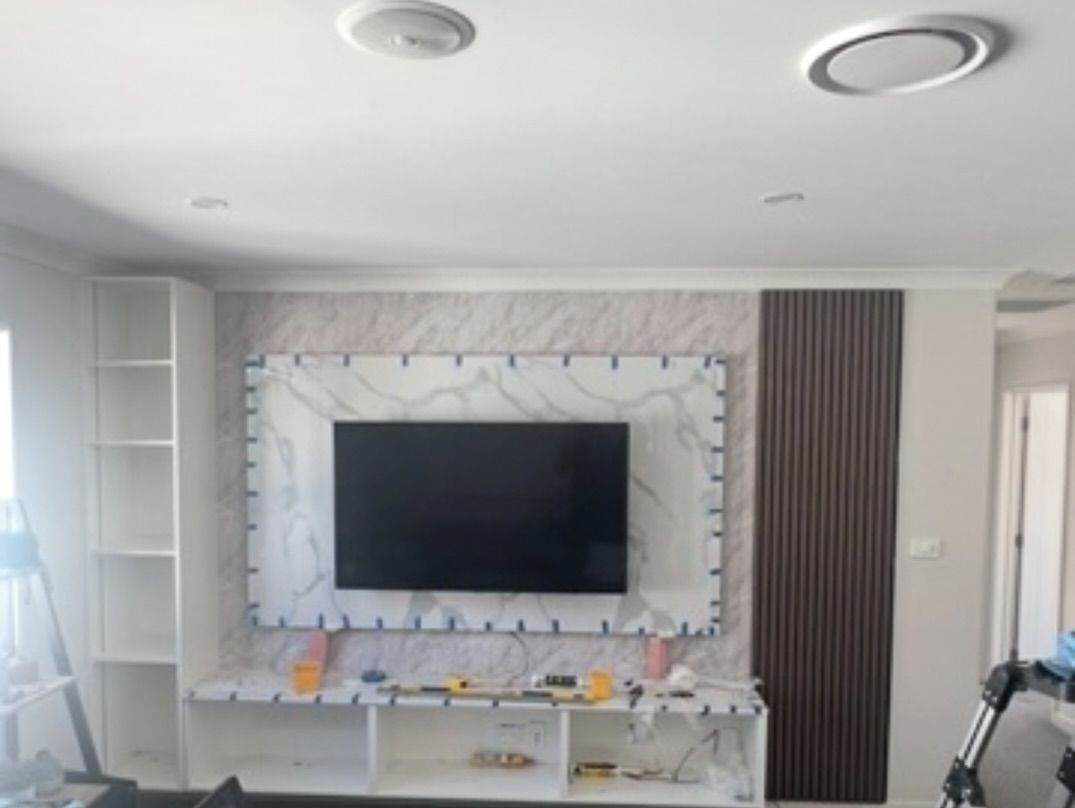 A living room with a TV mounted on a decorative marble wall, next to a vertical wooden panel and a white shelving unit.