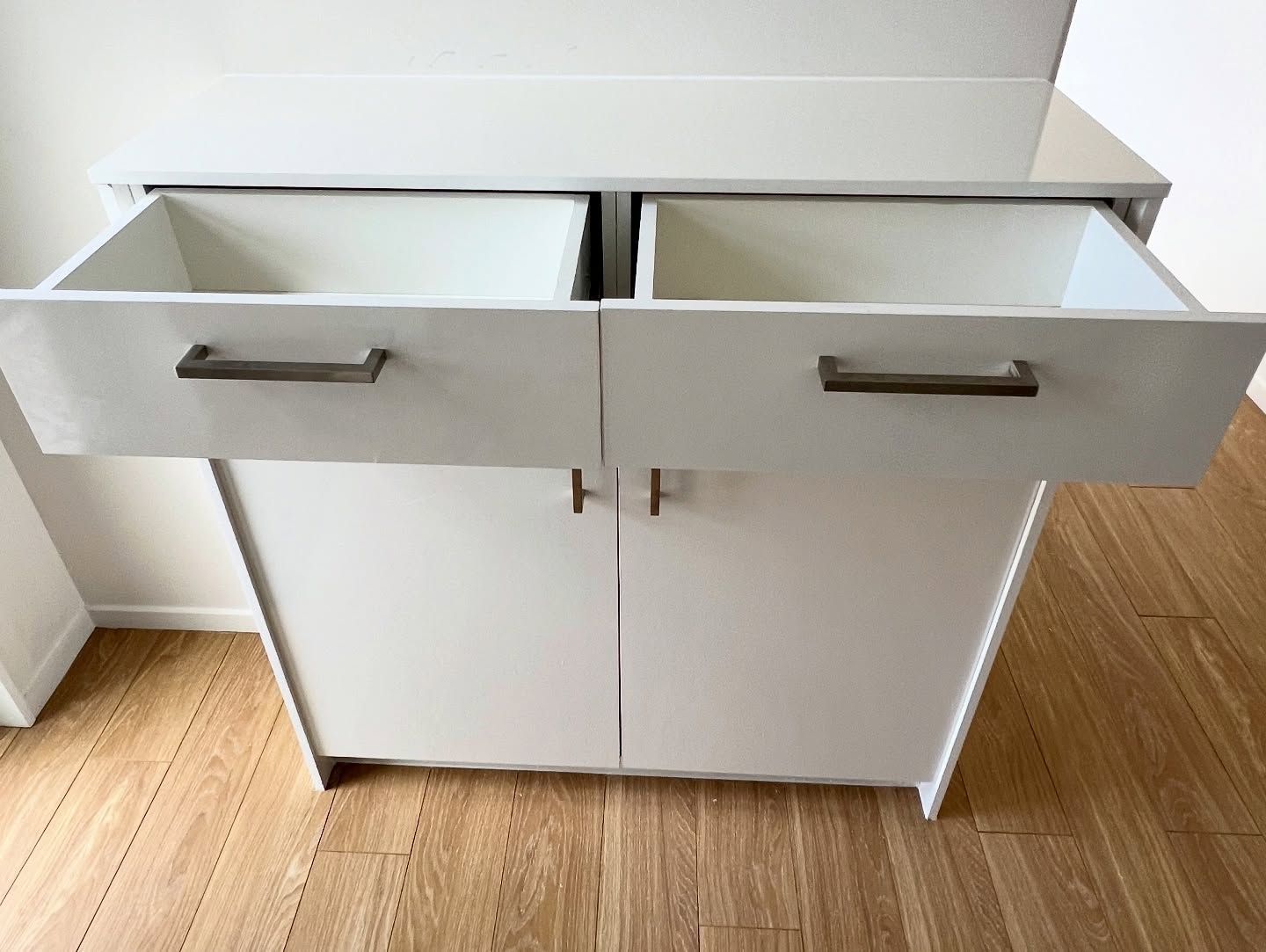 White cabinet with two open drawers above two closed doors, on a wooden floor.