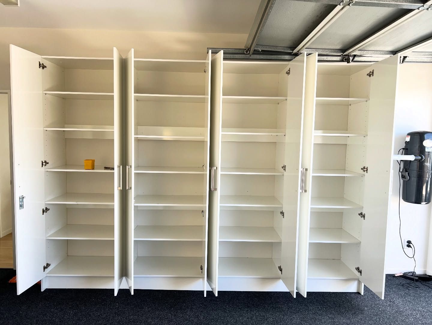 White storage cabinets with open doors against a garage wall, showing multiple shelves.
