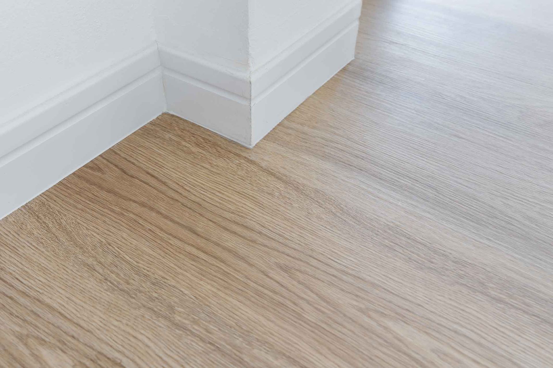 Corner of a room with white baseboards and light wood-look flooring.