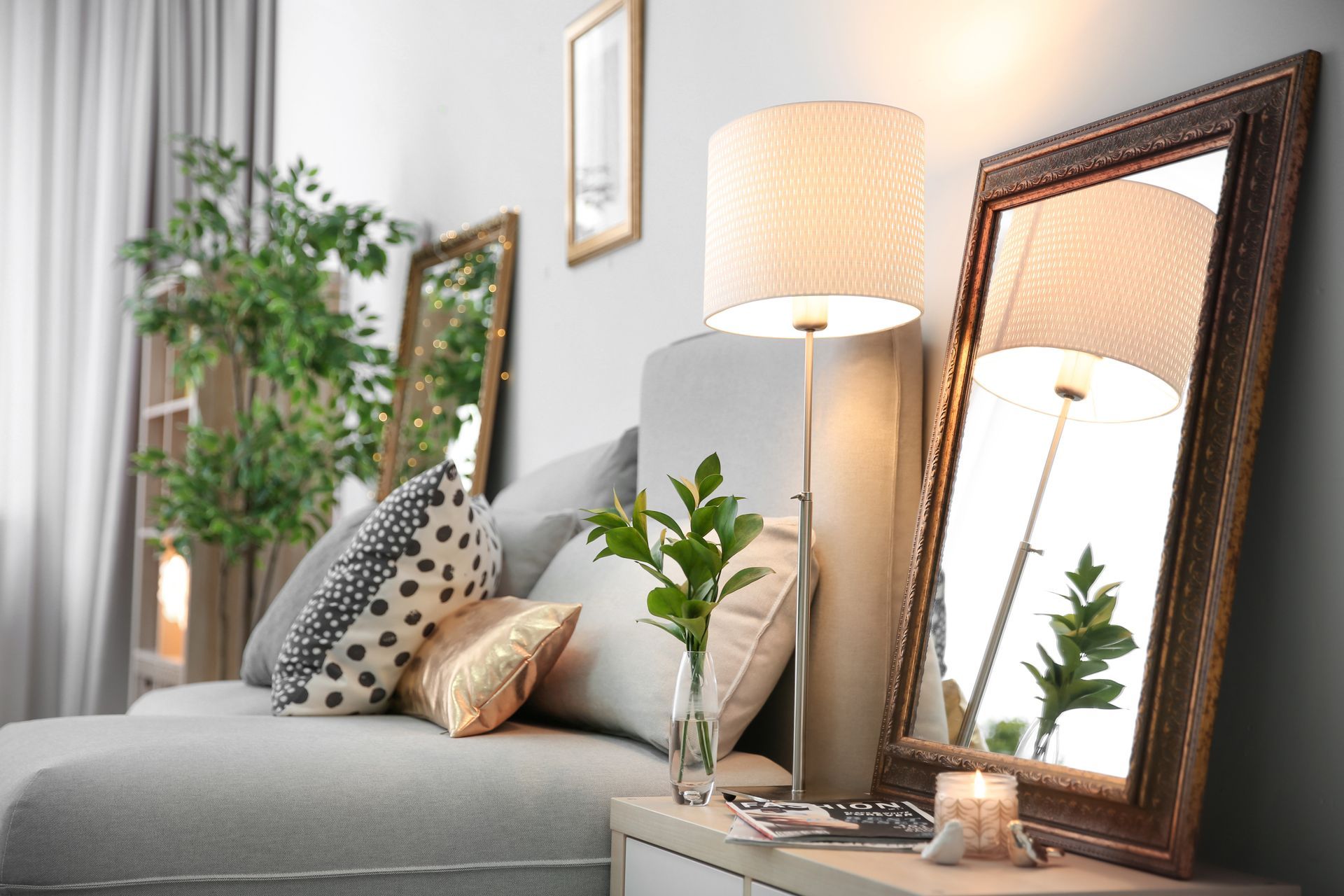 Cozy living room with a couch, mirrors, and a floor lamp. Neutral tones, candles, and plants create a warm atmosphere.