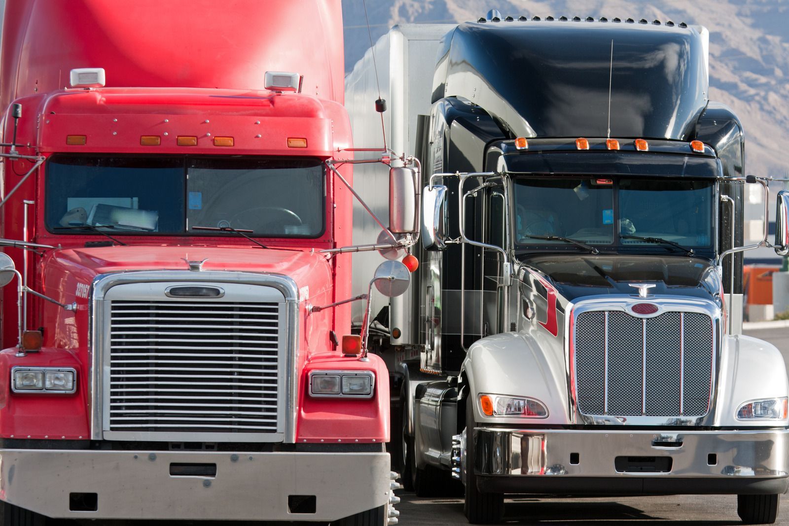 Two semi trucks are parked next to each other in a parking lot.