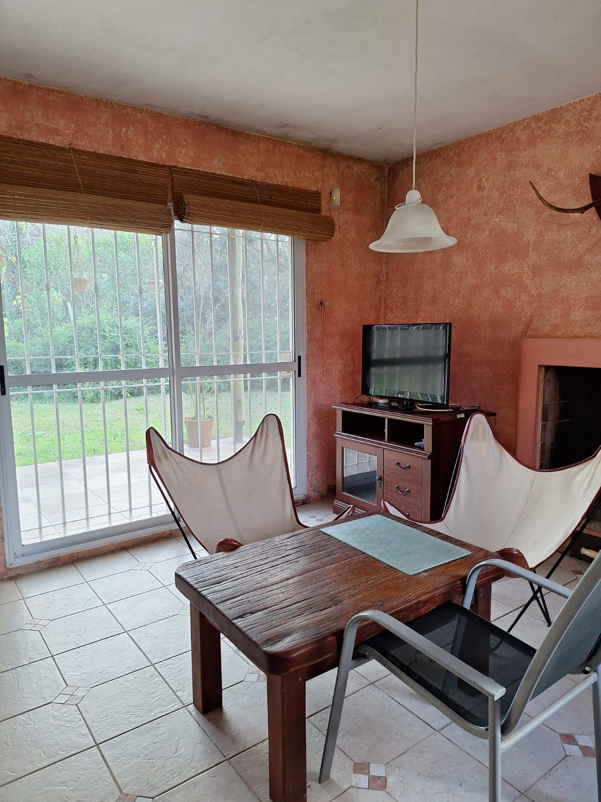 Una sala de estar con una mesa, sillas mariposa y un televisor cerca de una puerta corrediza que da a un patio.