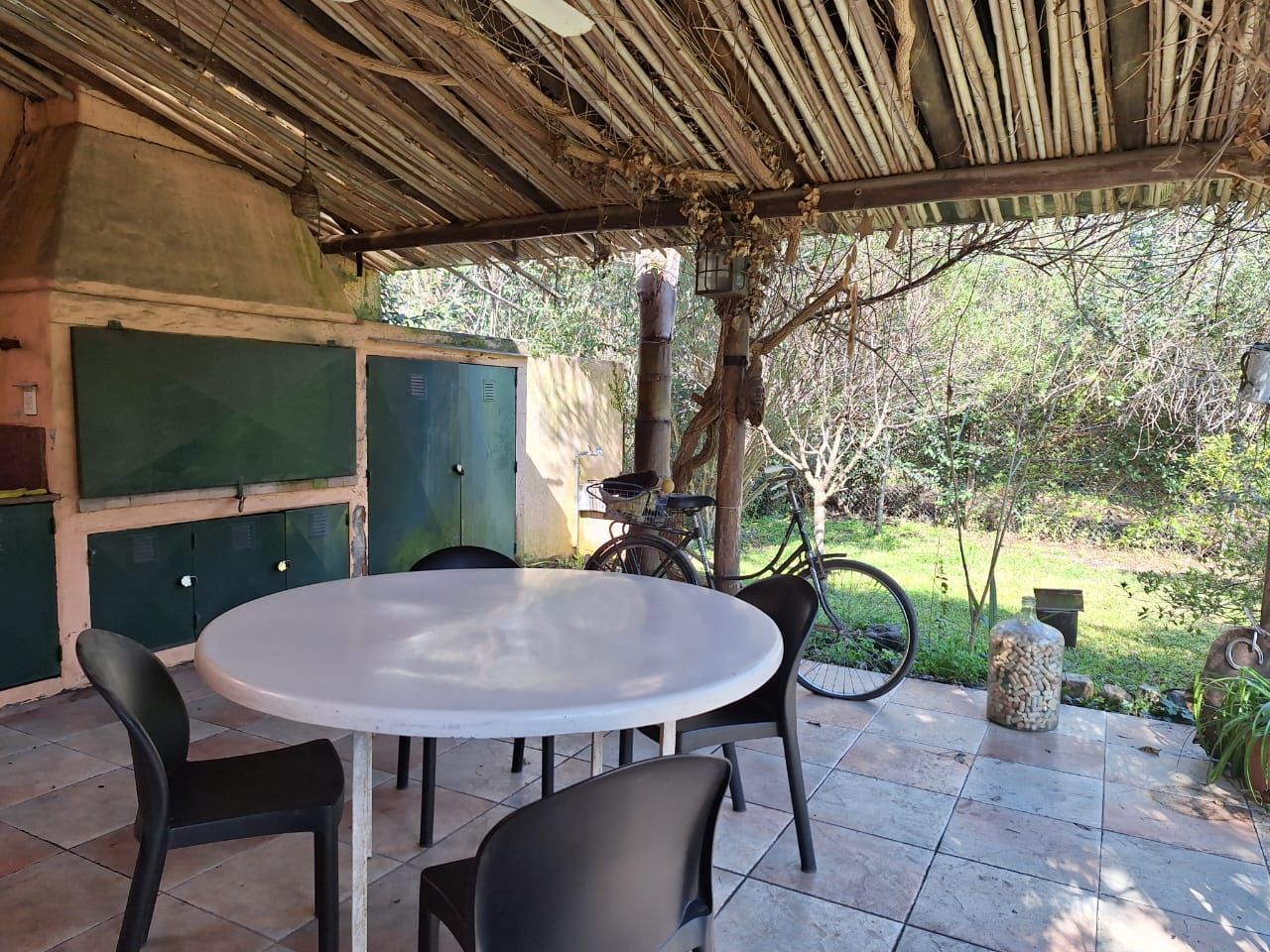 Comedor al aire libre con mesa blanca, sillas negras, barbacoa de ladrillo y bicicleta.