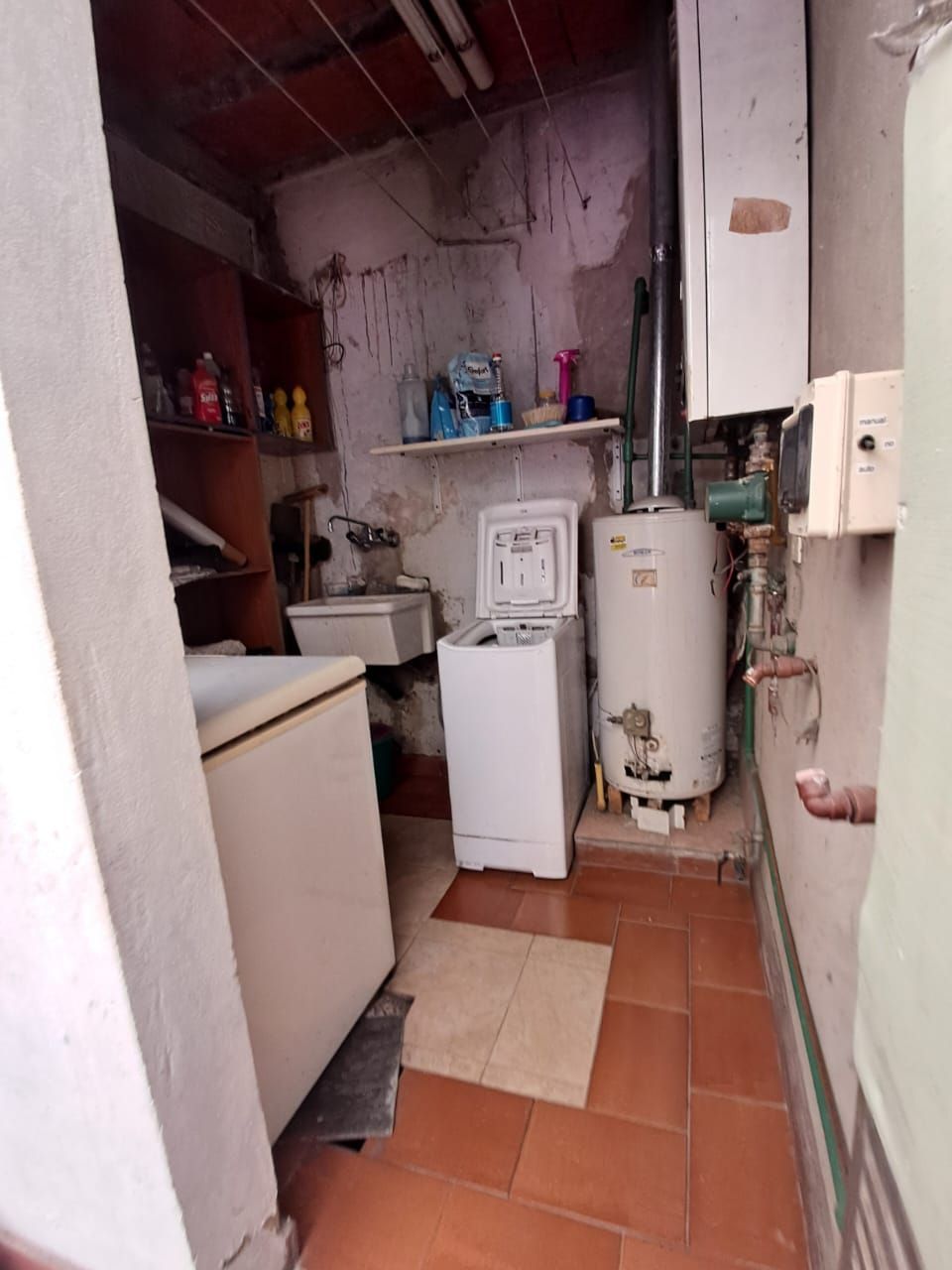 Cuarto de lavandería con lavadora, fregadero, calentador de agua, estantes y suelo de baldosas rojas.