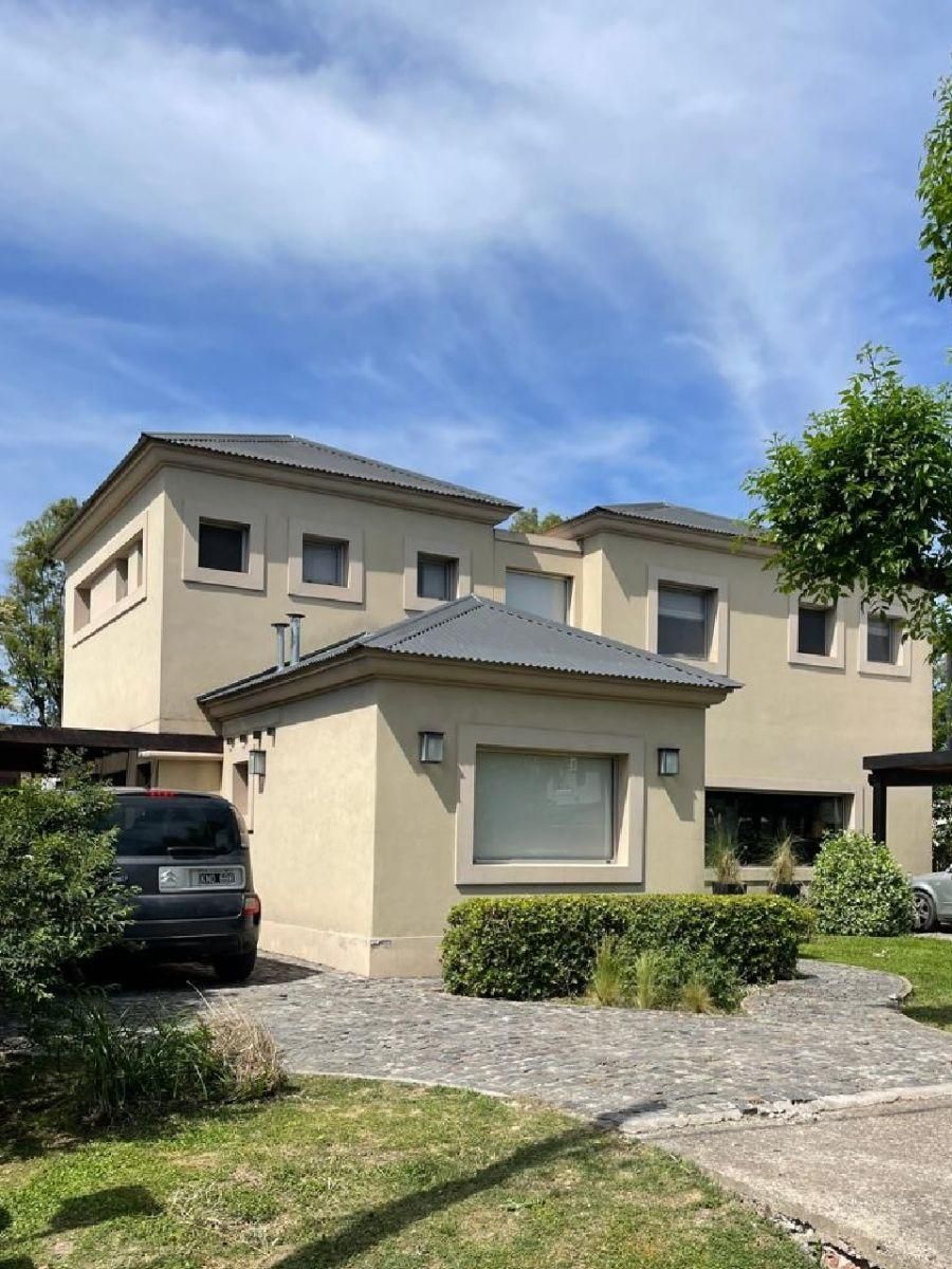 Casa de dos plantas color beige con una pequeña construcción independiente. Se ve el cielo azul
