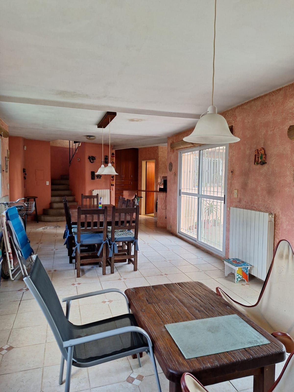 Comedor con escaleras, mesa, sillas, paredes rosas y una ventana.