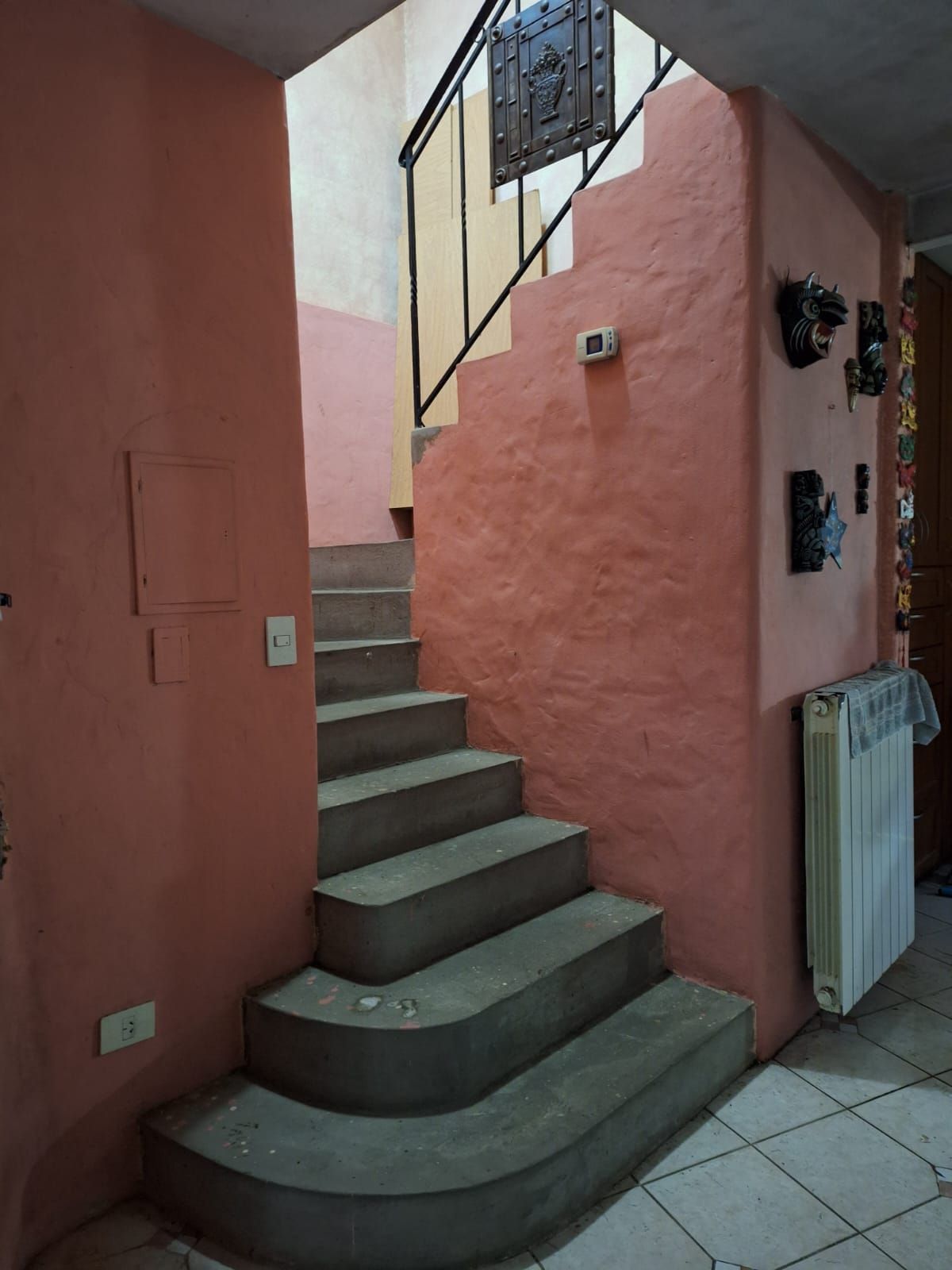 Escalera con peldaños de hormigón, paredes color melocotón y barandilla metálica. Un radiador a la derecha.