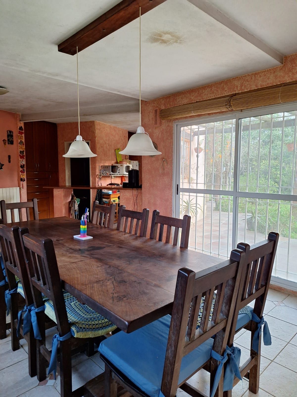 Comedor con mesa larga de madera, ocho sillas, dos lámparas colgantes y vistas al jardín.