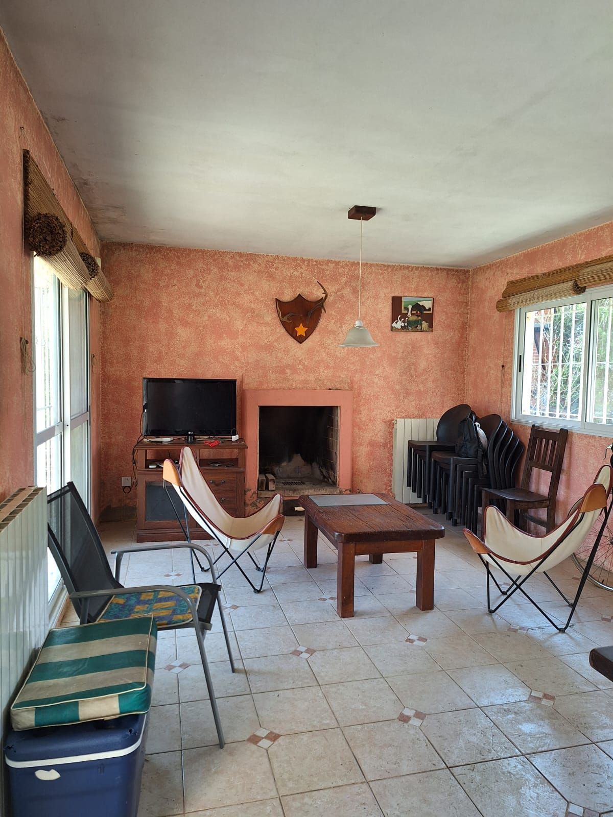 Salón con chimenea, televisión, sillones mariposa y una mesita de madera. Paredes rosas, suelo de baldosas.