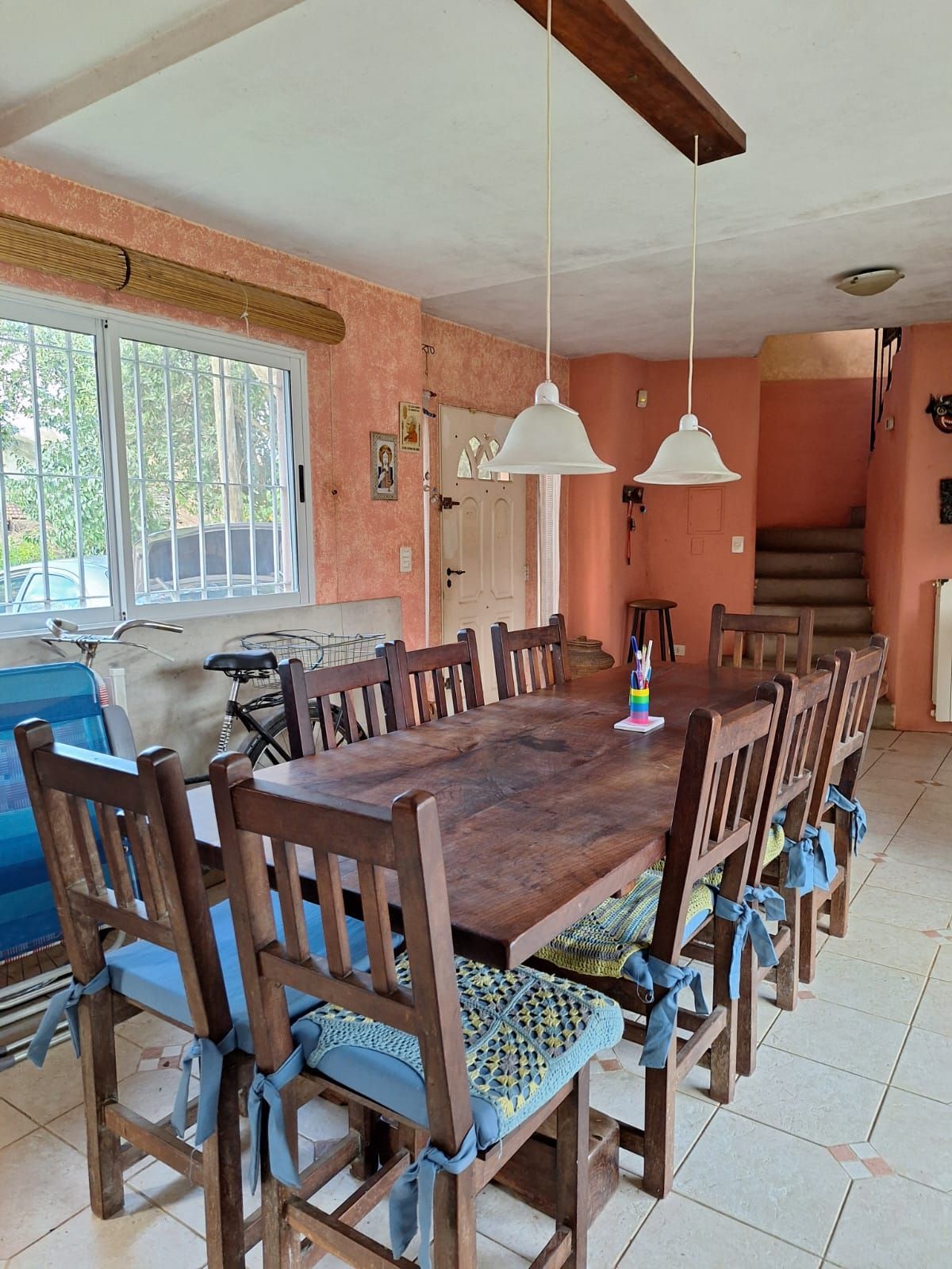 Comedor con mesa y sillas grandes de madera, paredes color melocotón y dos lámparas colgantes.