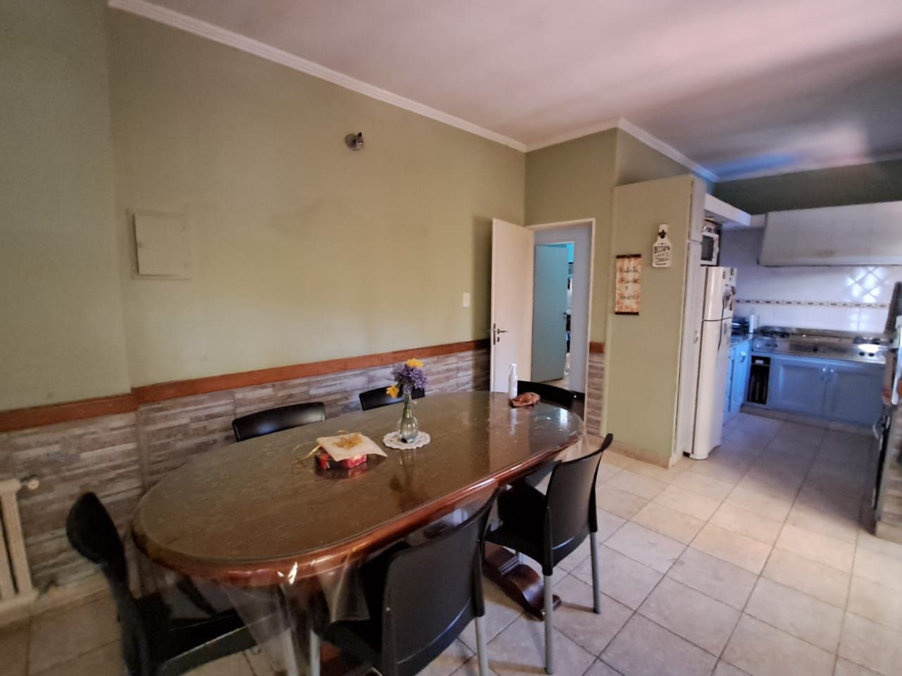 Comedor con mesa y sillas, que da a la cocina. Paredes verde claro y suelo de baldosas.