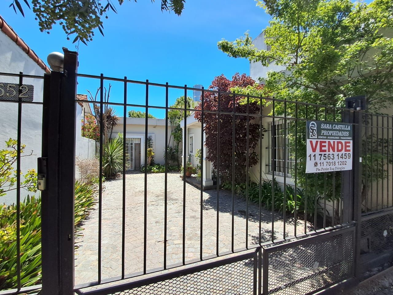 Portón negro frente a una casa en venta. Letrero que dice