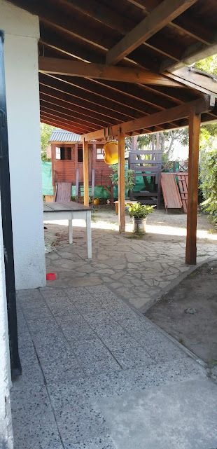 Patio con vigas de madera, mesa y un parque infantil al fondo.