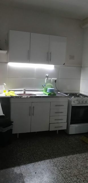 Cocina con armarios blancos, fregadero, estufa e iluminación fluorescente.