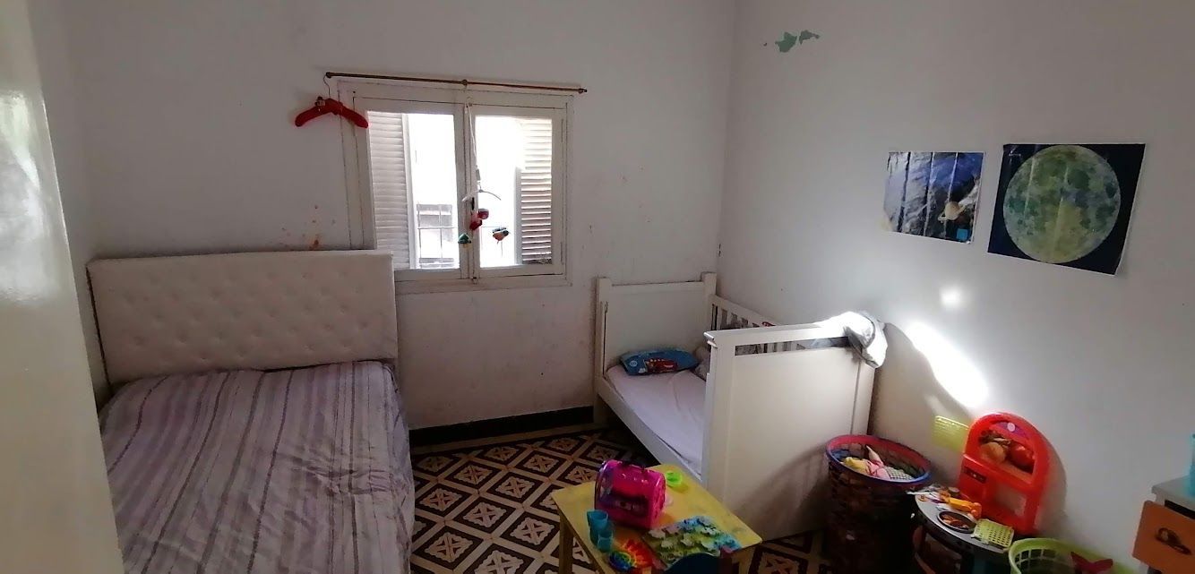 Un dormitorio pequeño con dos camas, una ventana y juguetes infantiles esparcidos por el suelo.
