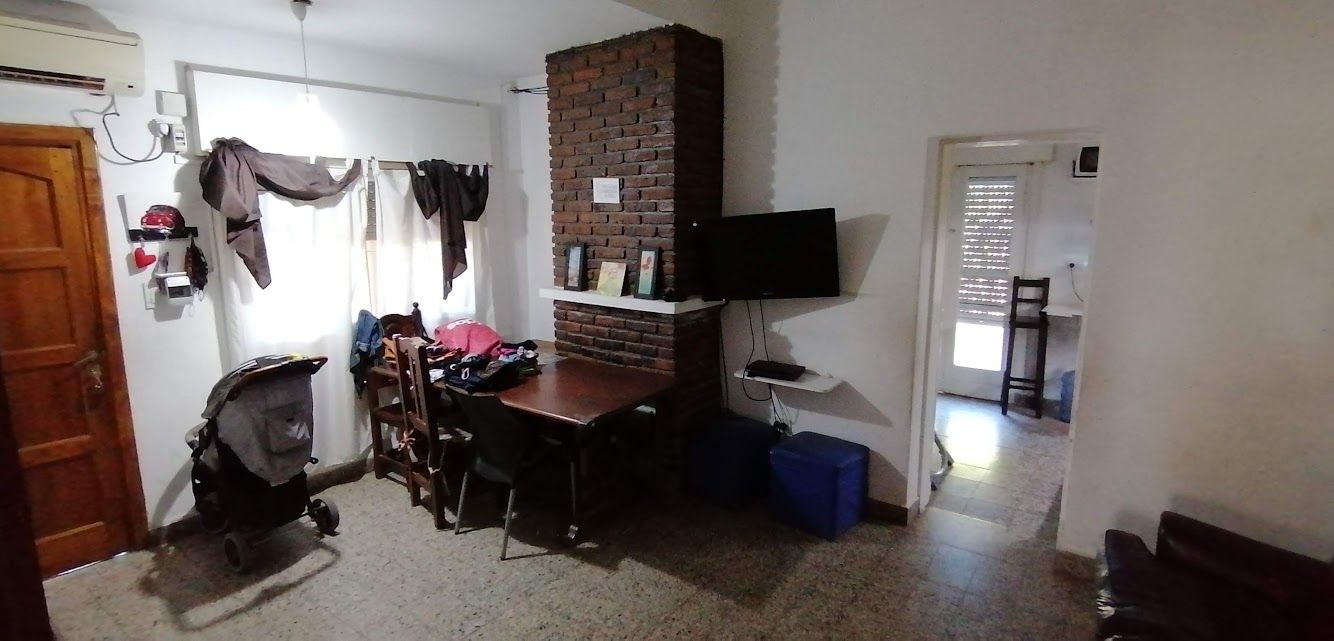 Sala de estar con puerta de madera, chimenea de ladrillo, mesa, televisor, cochecito de bebé y entrada.
