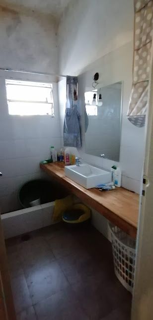 Baño con lavabo, espejo y encimera de madera. A la derecha hay una cesta de la ropa blanca y a la izquierda, una ducha.