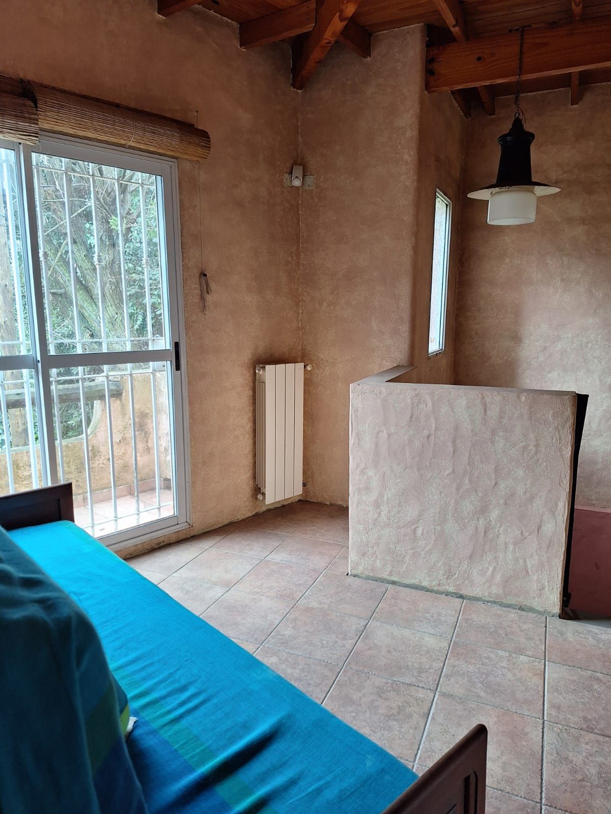 Habitación interior con sofá azul, ventana con rejas metálicas y pared marrón.