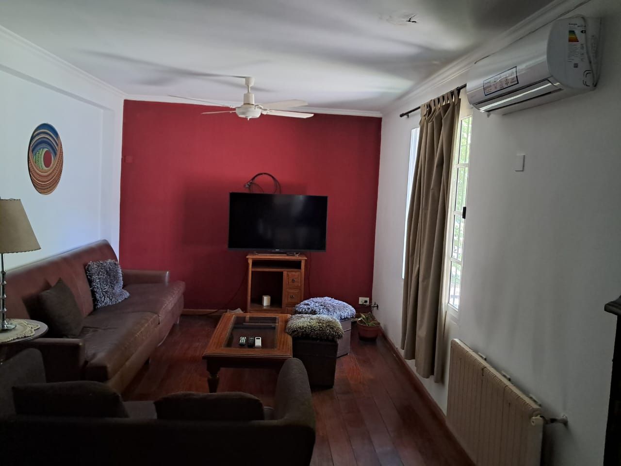 Sala de estar con sofá marrón, pared decorativa roja, televisor y aire acondicionado.