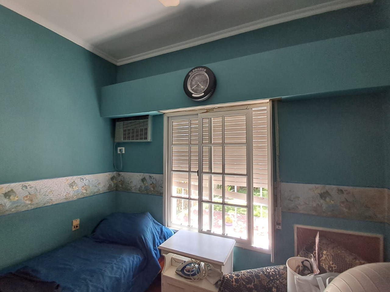 Habitación pequeña pintada de color verde azulado con una cama individual, ventana con persianas