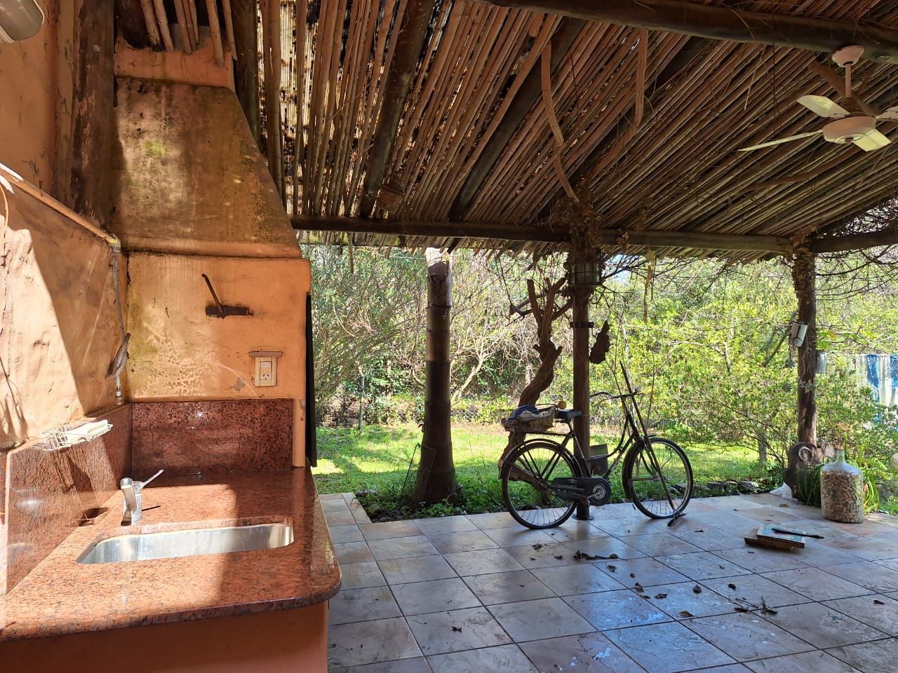 Cocina exterior con fregadero, encimera y bicicleta en un patio alicatado. Pérgola de madera con materiales naturales.