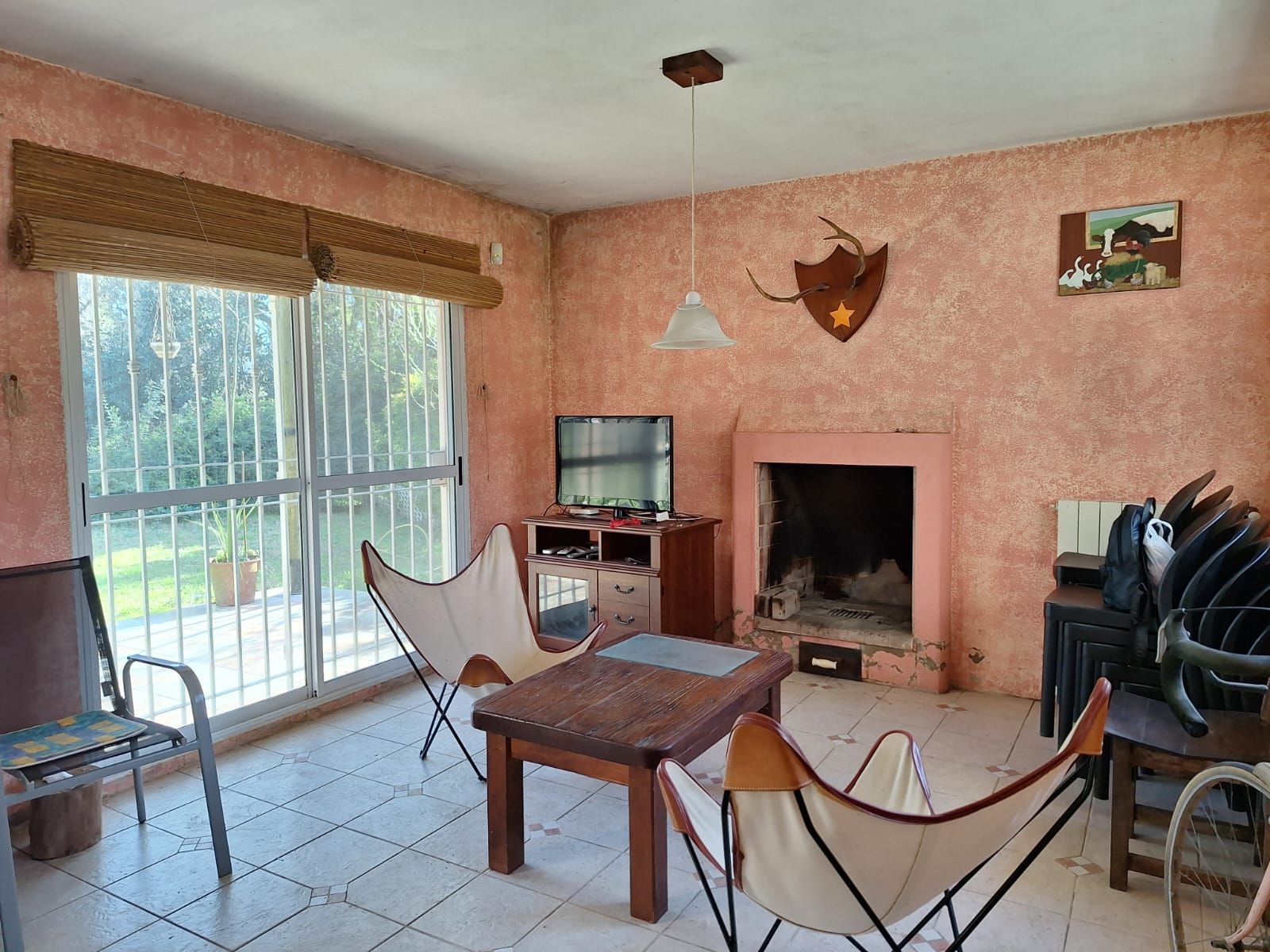 Sala de estar con paredes texturizadas de color rosa, chimenea, sillas con forma de mariposa y puerta corrediza de vidrio.