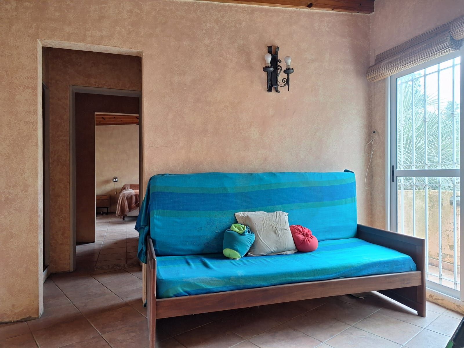 Sala de estar con sofá azul, puerta abierta a los dormitorios y puerta corredera de cristal a un balcón.